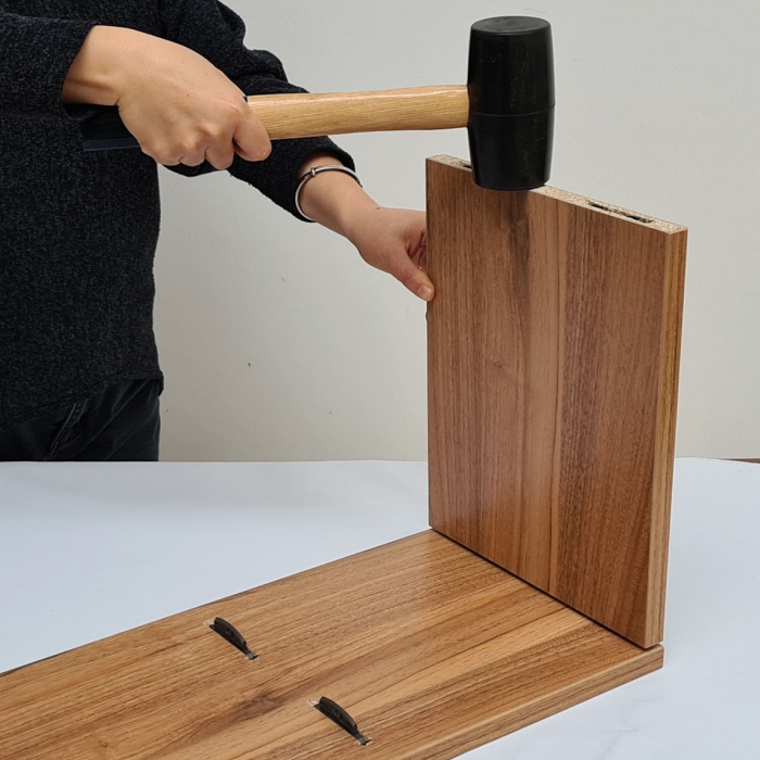 A hammer striking down on the FIYU® connector, seamlessly joining two pieces of wood. The image illustrates the easy assembly and sturdy connection of woodwork using the revolutionary FIYU®.